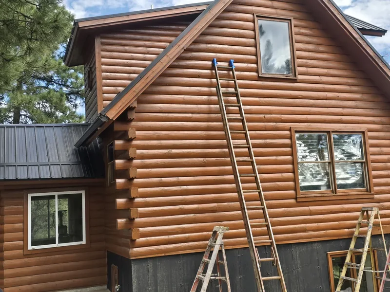 Log cabin exterior mid-restoration with ladders staged against the timber walls