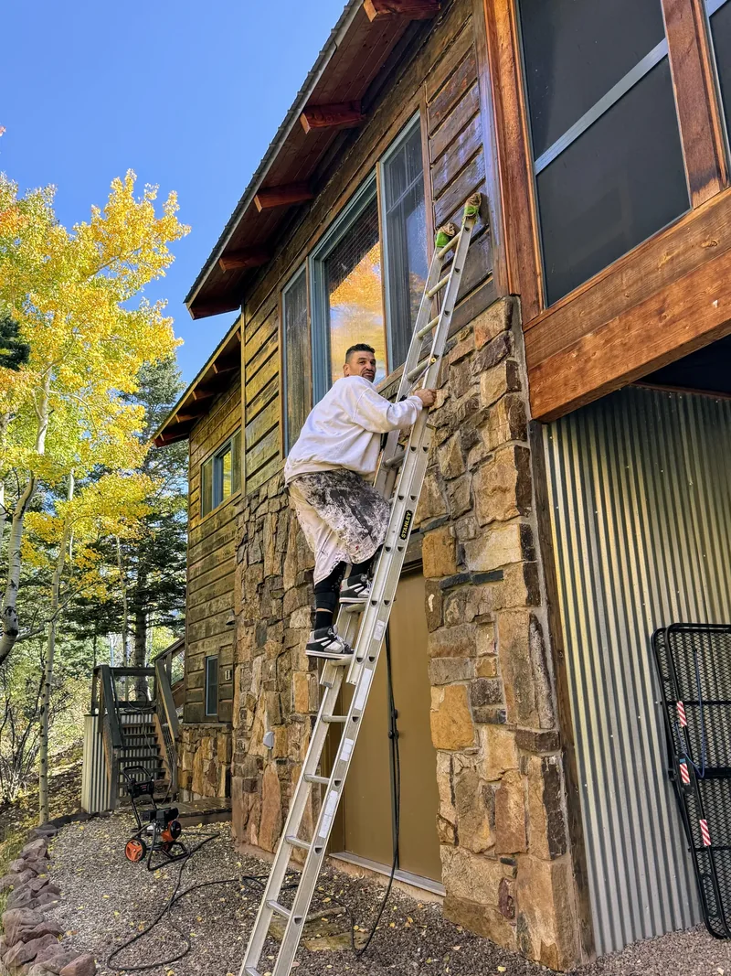 Painter on a ladder brushing fresh stain onto a log home wall in autumn
