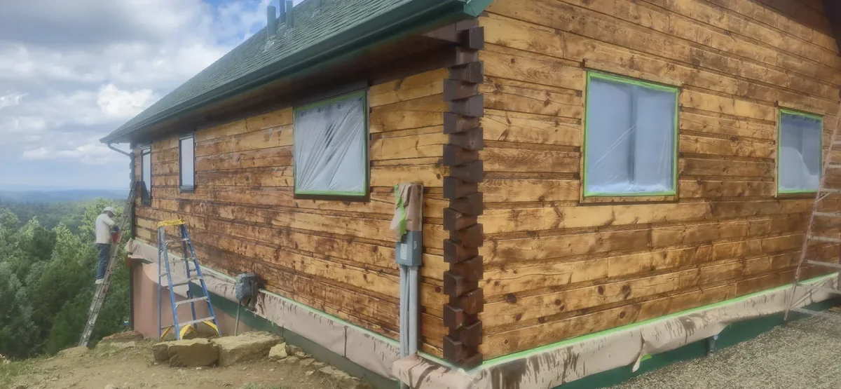 A weathered, graying log wall before SBJ Painting restored it